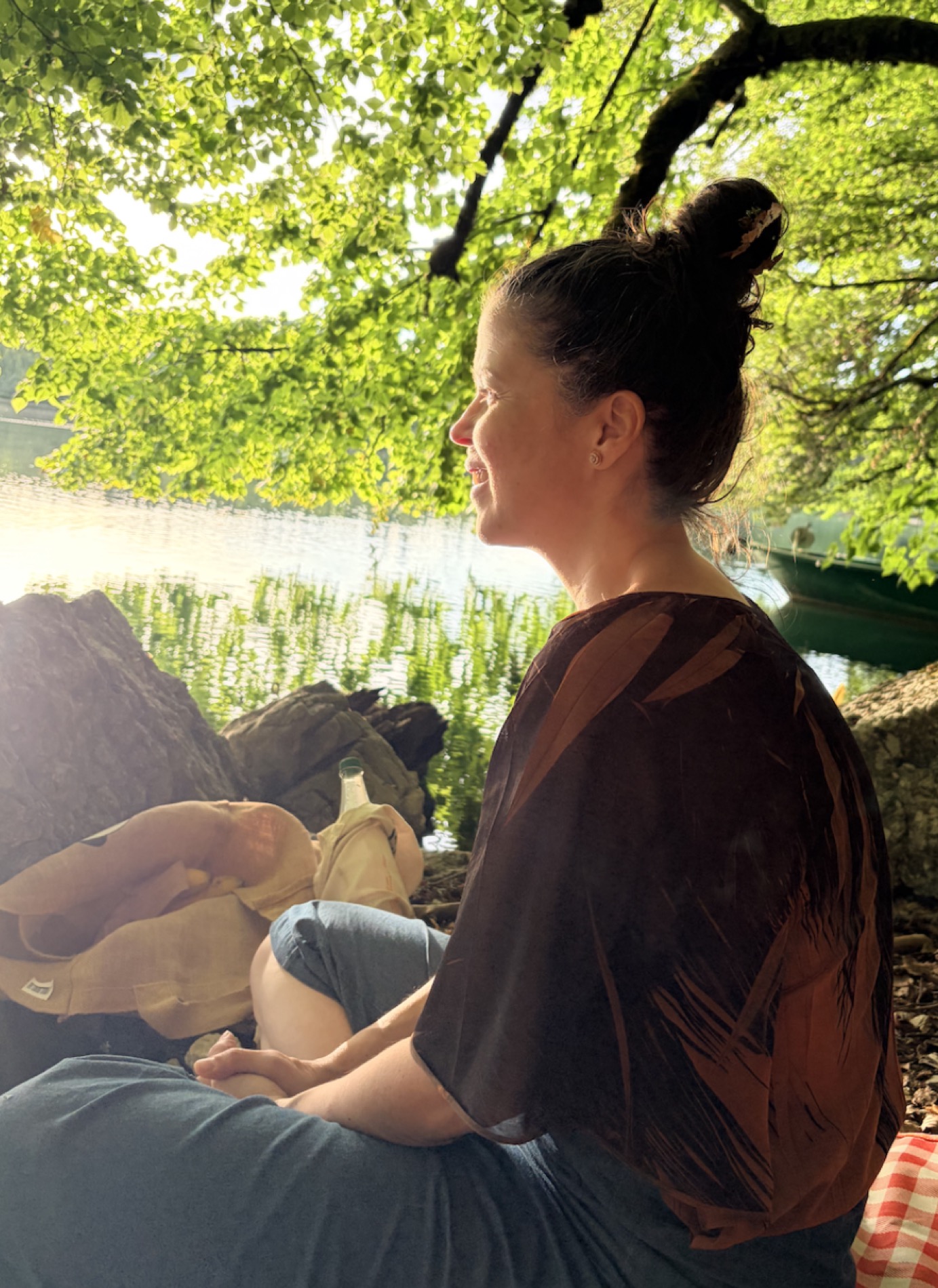 Une femme assise au bord du lac de Joux, sous les arbres, regardant l’eau.