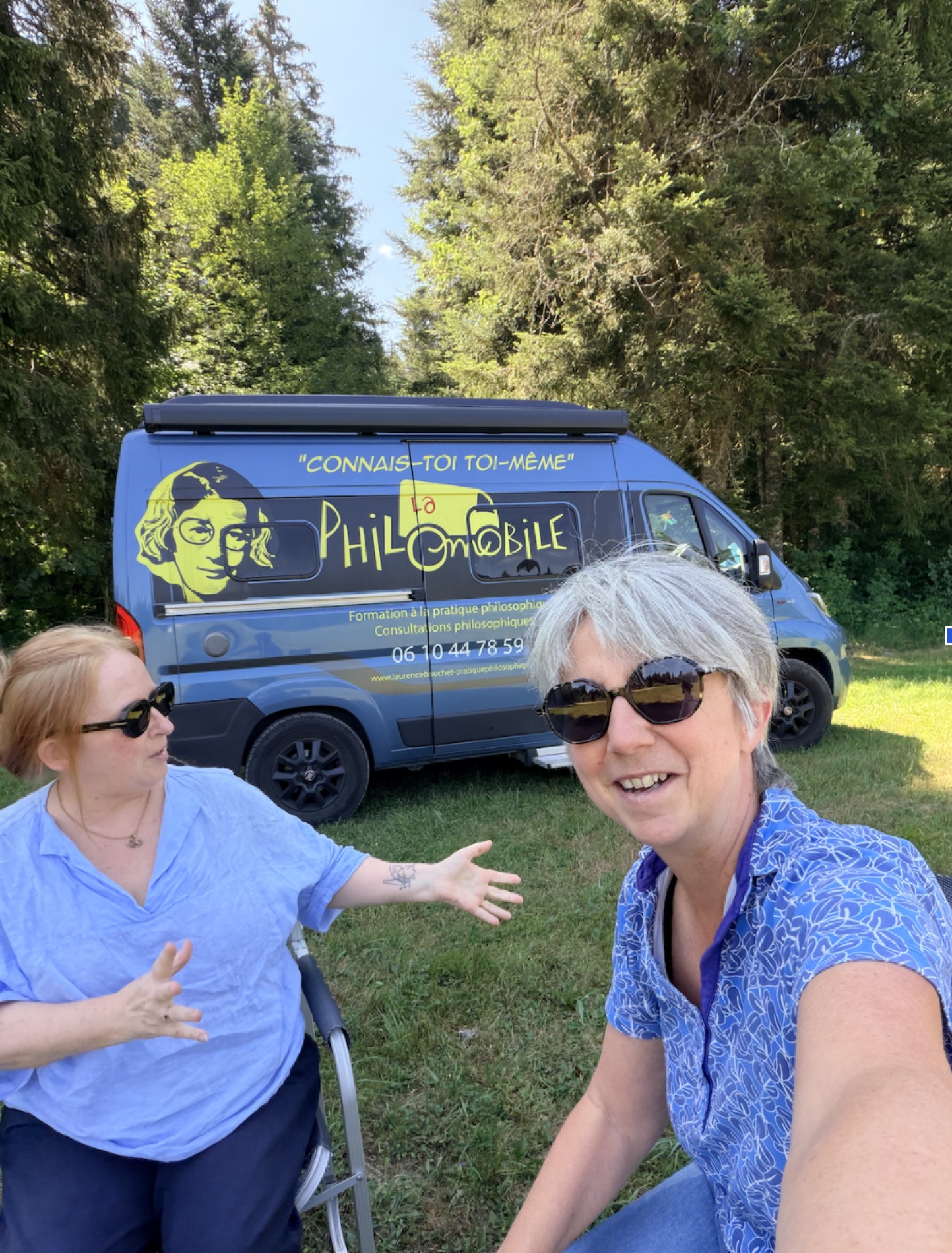 Laurence et une compagne de route, devant la Philomobile, sur l’herbe.