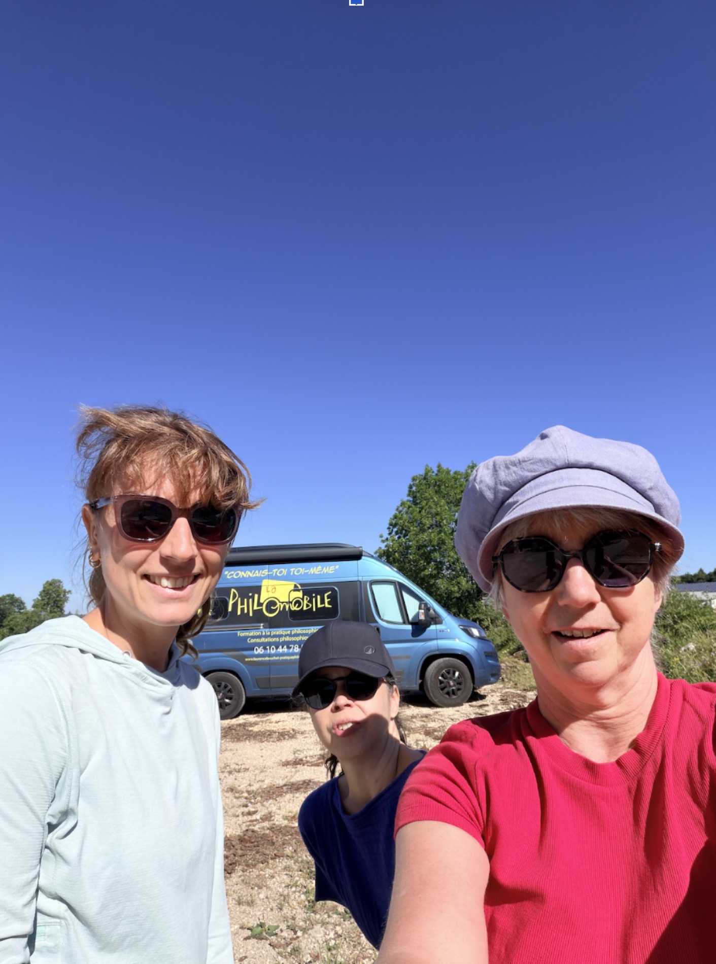 Laurence et deux compagnes de route, souriantes, devant la Philomobile sous un grand ciel bleu.